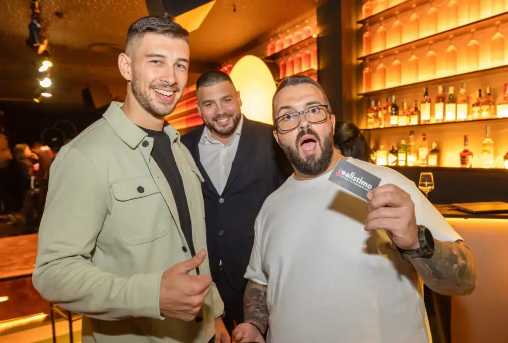 Сделка на ръба – Live Broker Show 38 Трима брокери позират на бара в Sotto Bar, единият показва визитка на Realistimo