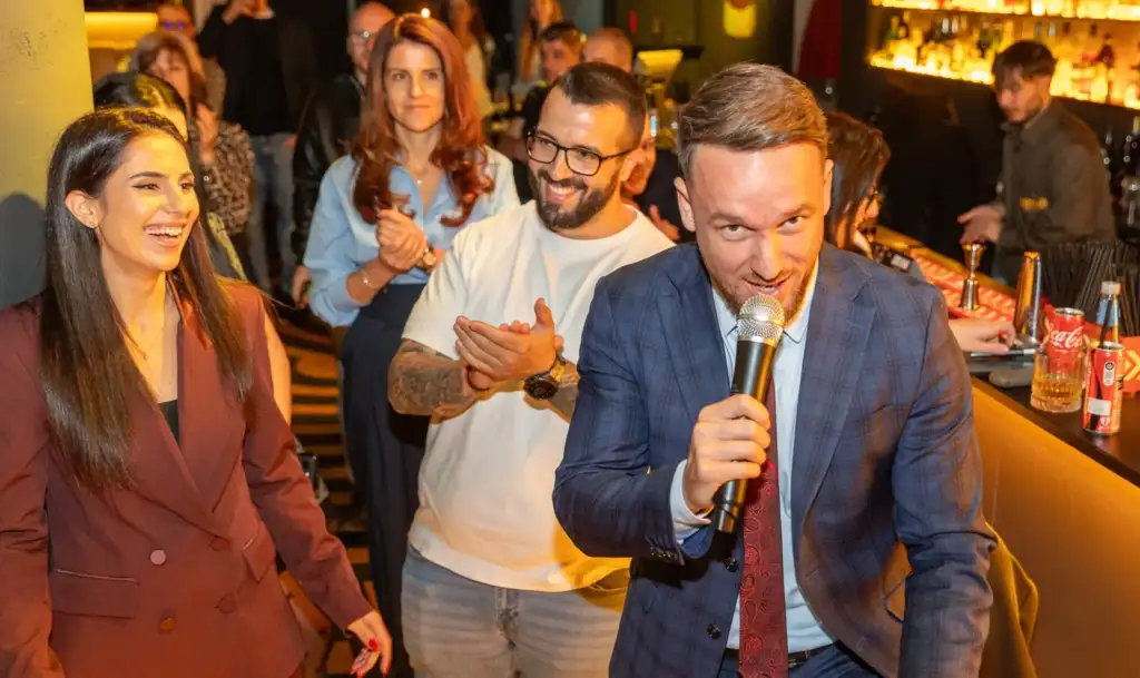 Сделка на ръба – Live Broker Show 60 Водещият говори в микрофона сред публиката, а колеги ръкопляскат