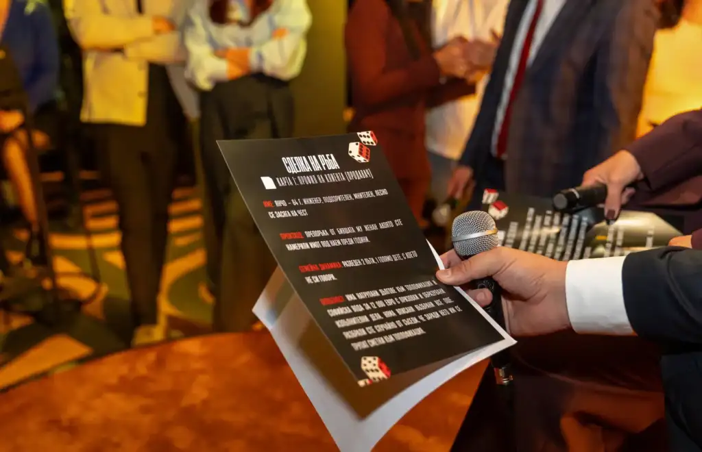 Сделка на ръба – Live Broker Show 5 Карта с казус „Карта 1: Профил на клиента (продавач)“ в ръката на участник с микрофон